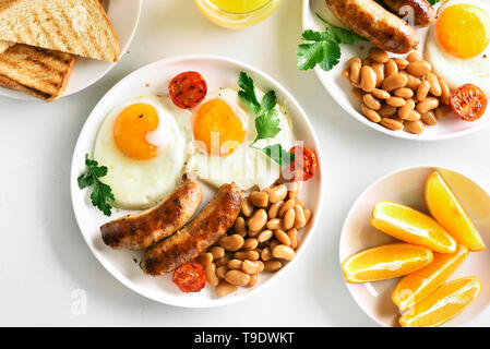 Morning food. Breakfast with fried eggs, sausages, beans, tomatoes, greens on plate over white stone background. Top view, flat lay Stock Photo