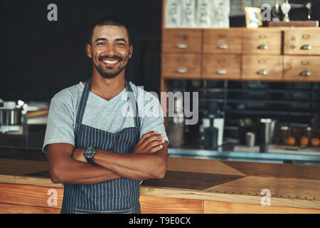 Young smiling barista posing near the counter at his cafe Stock Photo
