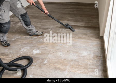 A man sucks water from the tiled floor with the vacuum cleaner. Stock Photo