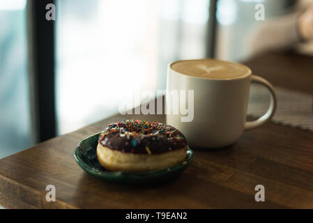 coffee with a heart made of milk and a donut on a wooden table. Bad breakfast Stock Photo