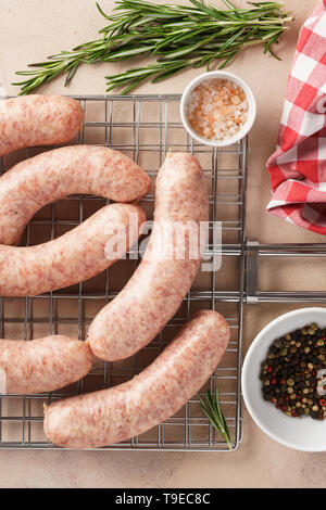 Raw sausages on grill grate with herbs and spices. Ingredients for barbecue. Overhead. Stock Photo