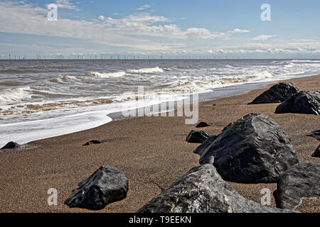 Beach in Lincolnshire,UK, with rocks and sea, and an offshore wind farm on the horizon Stock Photo