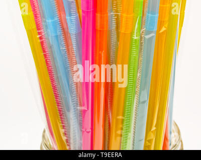 Many multicolored plastic straws in a glass bowl. Isolated on white background. Plastic straws are being banned in various countries around the world. Stock Photo