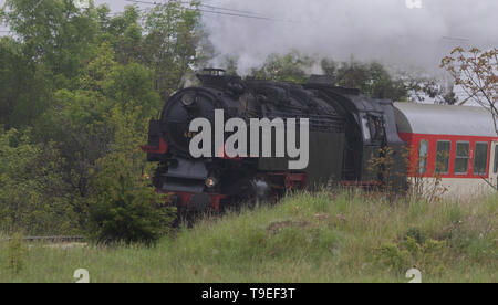 Historic steam locomotive with passenger wagons speeding on railroad tracks curve and blowing heavy white smoke near Sofia Stock Photo