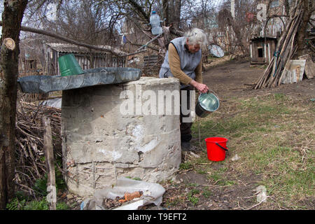 An old woman in a deserted village is gathering water from a well in a bucket, living alone. Stock Photo