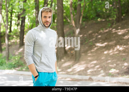 Taking minute break. Runner workout outdoor. Man athlete with hood after running outdoor, nature background. Athletic man relaxing break. Athlete hood Stock Photo