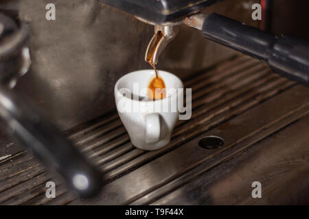 Coffee cup on an espresso machine and coffee drip in a cup. Process of making espresso coffee on the old machine in a pub kitchen. Close up Stock Photo