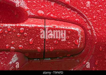 Concept image of water droplets on a bright red car door handle and surrounds suggesting a passage to warmth, comfort and dryness. Stock Photo