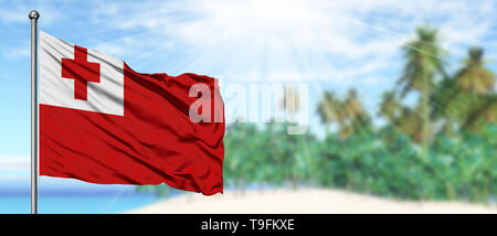 Waving Tonga flag in the sunny blue sky with summer beach background. Vacation theme, holiday concept. Stock Photo