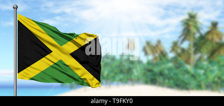 Waving Jamaica flag in the sunny blue sky with summer beach background. Vacation theme, holiday concept. Stock Photo