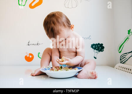 Baby eating by himself learning through the Baby-led Weaning method, exploring the flavors of food with curiosity. Stock Photo