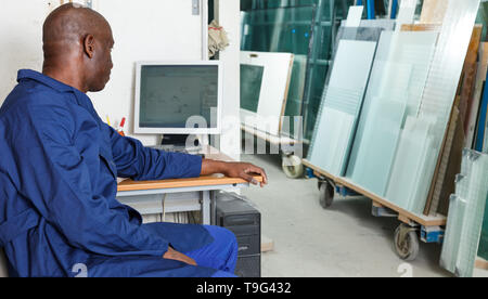 concentrated glass factory worker sitting at workplace with computer, controlling technical process in workshop Stock Photo