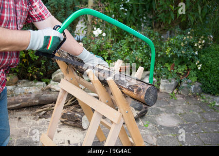 Sawing firewood manually with a hacksaw on a wooden sawhorse Stock Photo