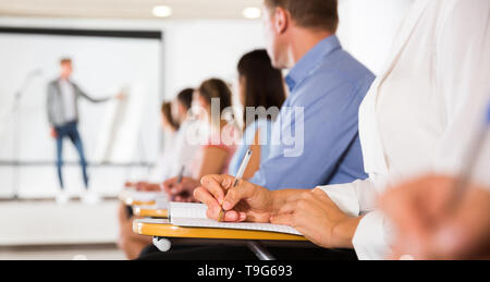 Woman making notes during lecture, focus on female hand with pen Stock Photo