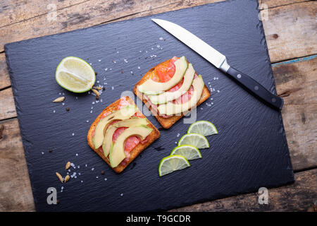 Fresh salmon sandwich with avocado and lime on black slate board. Stock Photo