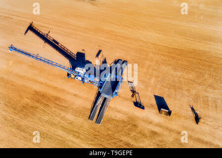 Grain bulk storage elevator site with mechanical loader processing tonnes of wheat and other grains in aerial overhead top down view. Stock Photo