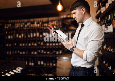 wine seller holding a bottle of wine at workplace. close up side view photo.man attend professional courses to become semmilier. education concept Stock Photo