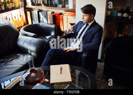 Young handsome serious man sitting on chair tasting cognac.close up side view photo.relaxation concept Stock Photo