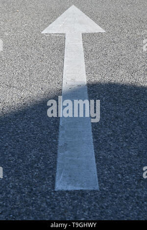 Asphalt sign: white arrow on the concrete texture exiting from shadow Stock Photo