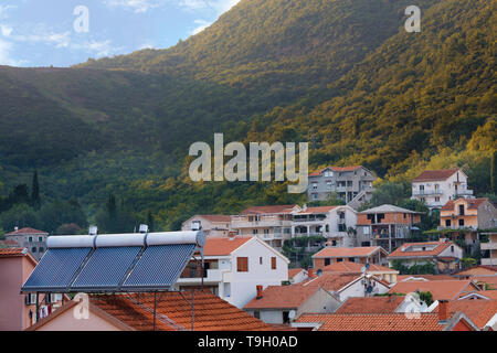 Modern renewable solar water heaters are installed on the orange tile roof of the house against the background of a mountain landscape in Montenegro Stock Photo