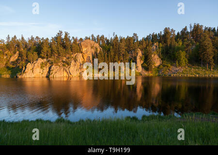 Golden sunshine in the late afternoon shines on a quartz rock formation and creates a soft reflection at Stockade Lake in Custer State Park, South Dak Stock Photo