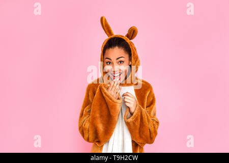 Young woman in bunny kigurumi standing isolated on pink background looking camera laughing playful Stock Photo