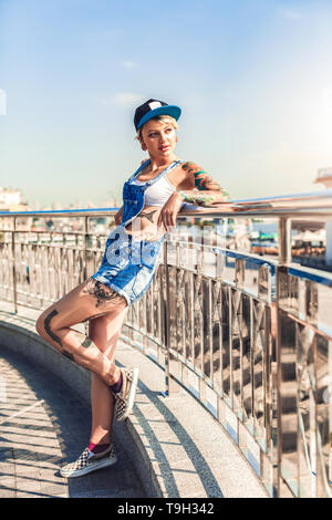 Young alternative girl wearing cap standing on the city street leaning back looking at city joyful Stock Photo