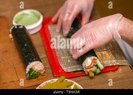 The process of making Japanese sushi. Knife in hand cuts a roll close-up on  a wooden board Stock Photo - Alamy