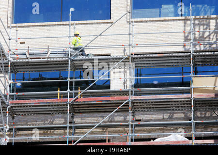 A new building under construction with a worker standing on the scaffolding. Stock Photo