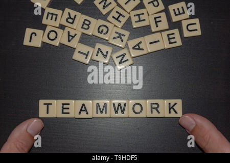 Tile letters with fingers spelling teamwork on a black background with mixed letters on top. Concept for business, personal, team other goal-setting Stock Photo