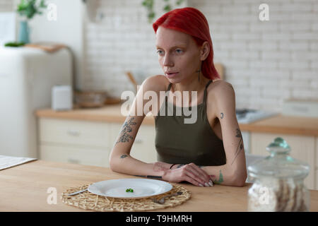 Anorexic woman looking awful sitting near plate with three peas Stock Photo