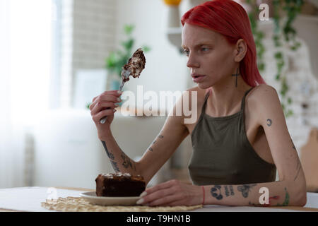 Tattooed skinny woman looking at big piece of dessert Stock Photo