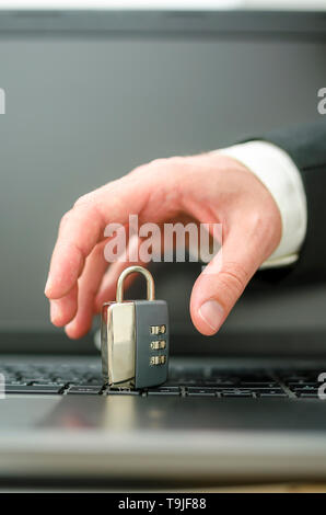 Hand of a hacker trying to steal a padlock from laptop keyboard. Stock Photo