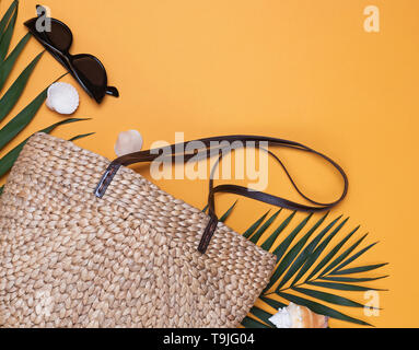 Stylish straw wicker bag, sunglasses and palm leaf. Creative summer composition on the yellow background. Stock Photo