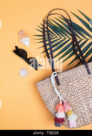 Stylish straw wicker bag, sunglasses and palm leaf. Creative summer composition on the yellow background. Stock Photo