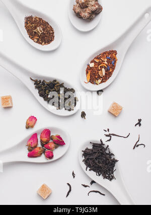 Different sorts of dry tea in white spoons on the white background, top view Stock Photo