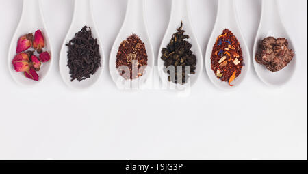 Different sorts of dry tea in white spoons on the white background, top view Stock Photo