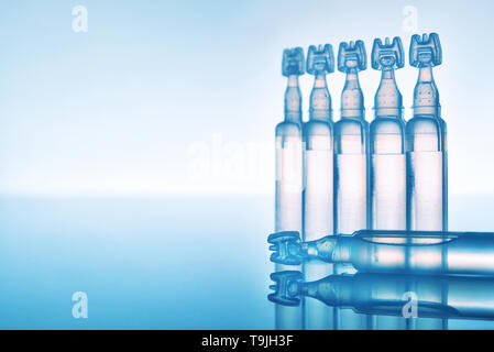 Artificial tears eye drops encapsulated in plastic pipettes and reflected on glass table with blue background. Horizontal composition. Front view Stock Photo