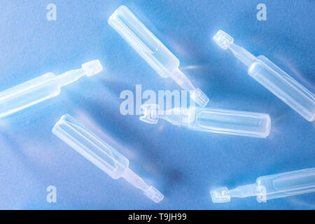 Artificial tears eye drops encapsulated in plastic pipettes and reflected on glass table with blue background. Horizontal composition. Top view. Stock Photo