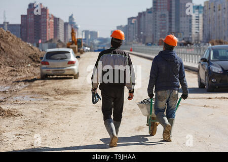 Two workers in helmets drive a wheelbarrow against the background of new buildings. Stock Photo