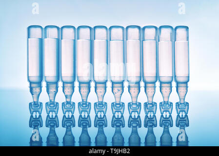Artificial tears eye drops encapsulated in plastic pipettes and reflected on glass table with blue background. Horizontal composition. Front view upsi Stock Photo