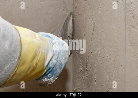 Hand with a spatula in the process of leveling the raw plaster. Stock Photo