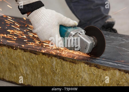 The hand of a worker in a glove cuts the building material with an angular grinding machine, creating sparks. Stock Photo