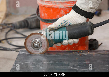The hand of a worker in a glove cuts the building material with an angular grinding machine, creating sparks. Stock Photo