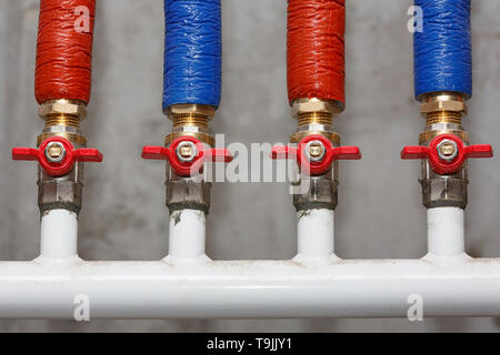 Sanitary cranes with water supply pipes, insulated with colored braids. Stock Photo