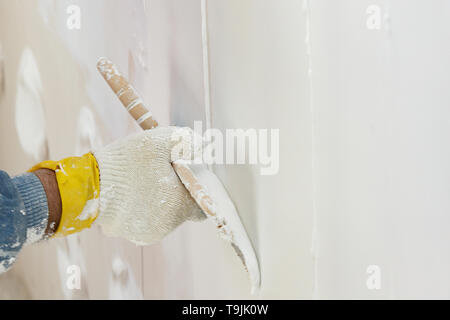 Hand with a spatula in the process of leveling the raw plaster. Stock Photo