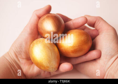 Three bright gold and bronze eggs in hands on a white background, Selective soft focus. Copy space. Stock Photo