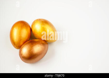Three gold and bronze Easter eggs on a white background. Selective soft focus. Copy space. Stock Photo