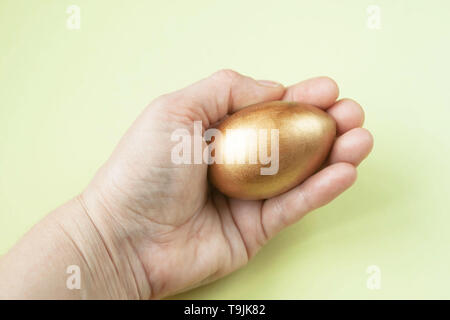 One single golden egg in the hand on light background. Text copy space. Selective soft focus. Stock Photo