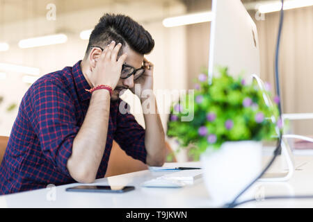 Tired and worried indian man at workplace in office Stock Photo